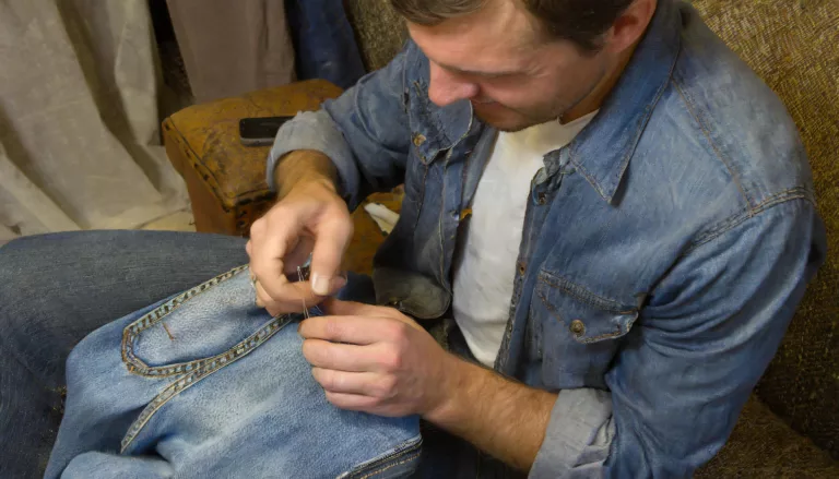 A man sewing a pair of jeans by hand